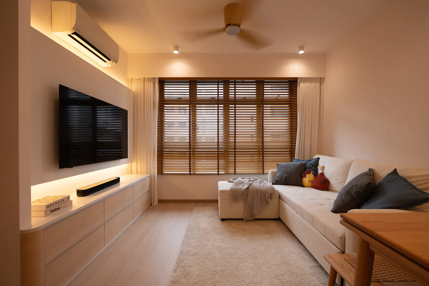 Warm and cozy living room with wooden blinds and a cream sofa designed by 9 Creation